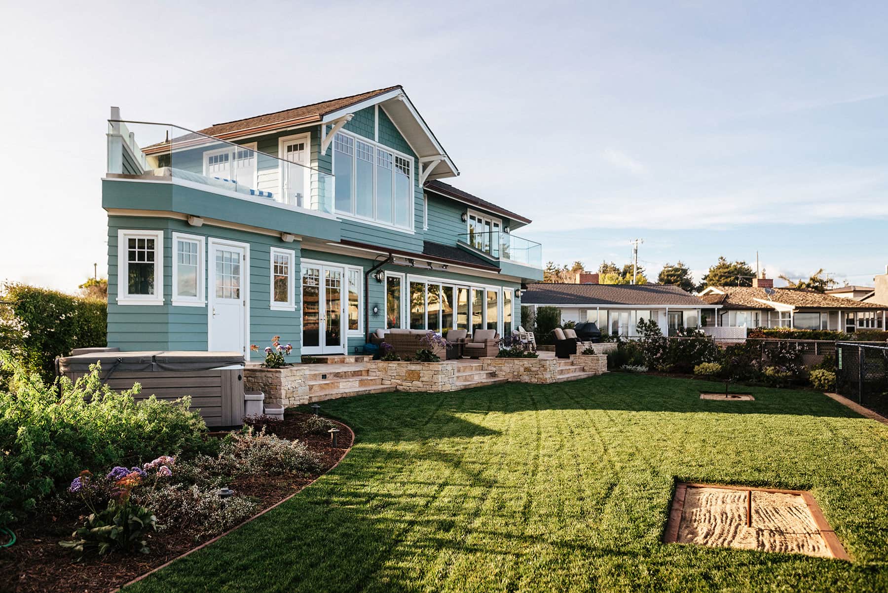 Backyard entertaining space with stone patio, lawn & ocean views installed by K&D Landscaping