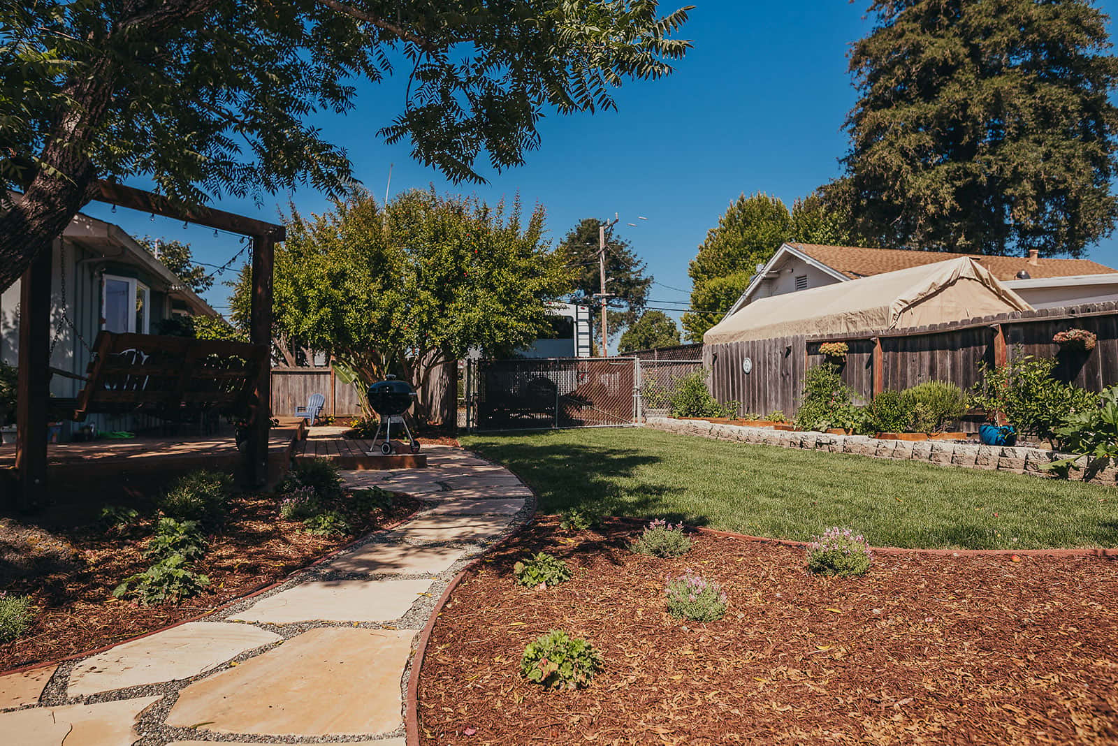 Backyard landscape featuring fruit-bearing trees, metal edging, lawn area, and mature shade trees installed by K&D Landscaping
