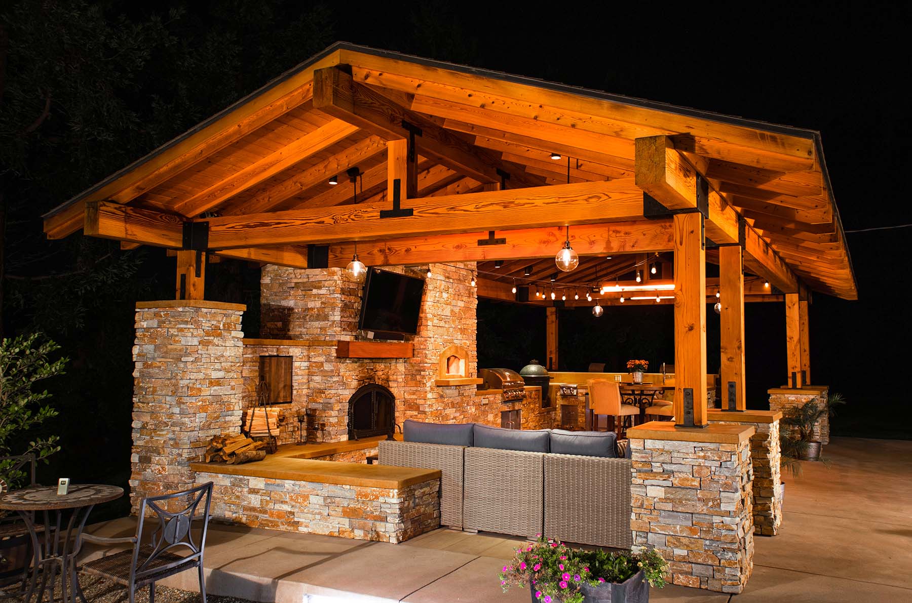 Custom outdoor kitchen pavilion featuring stone veneer, fireplace, pizza oven, and outdoor living space by K&D Landscaping