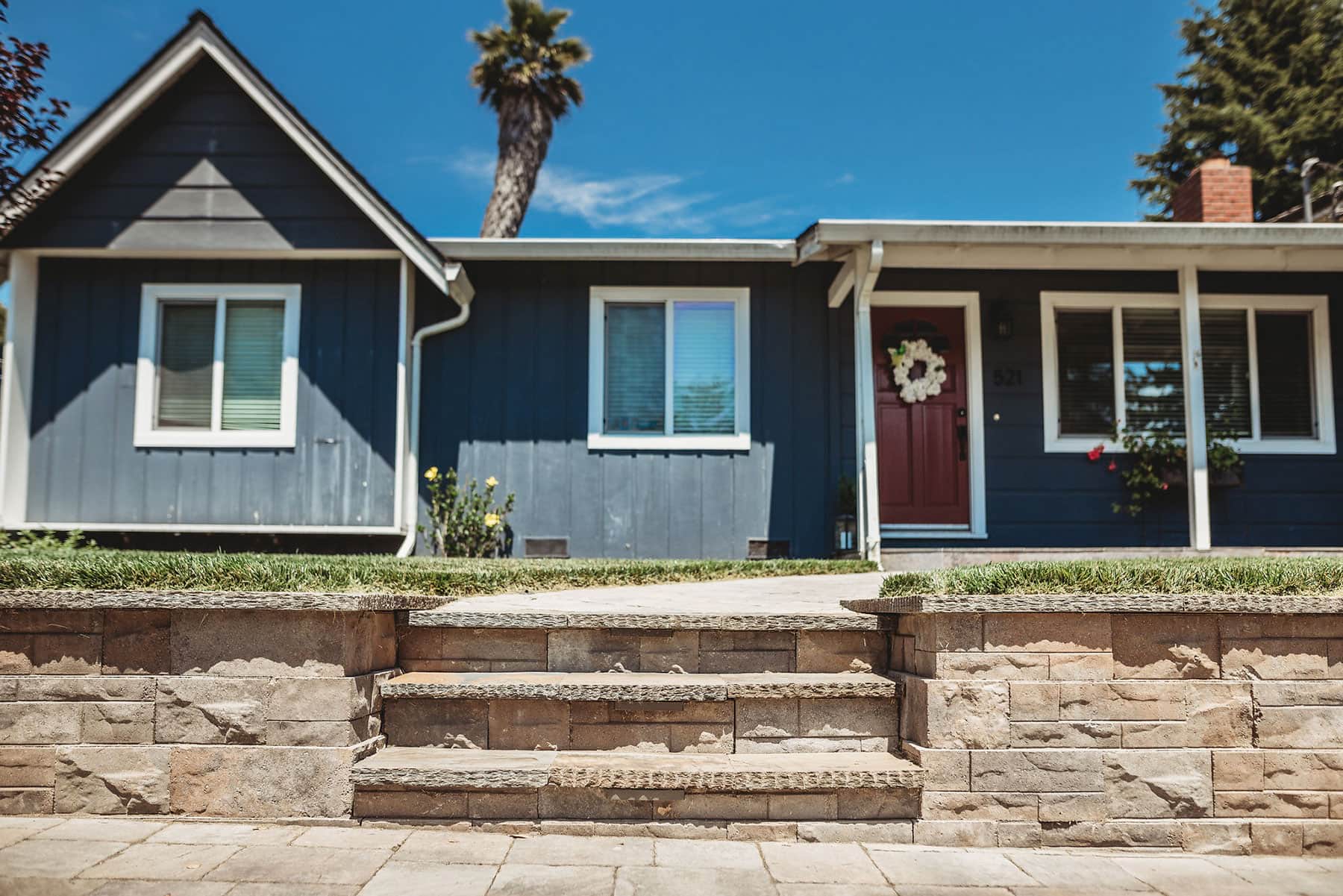 Front entryway with stone retaining wall stairs, paver walkway, lawn, and planting beds completed by K&D Landscaping