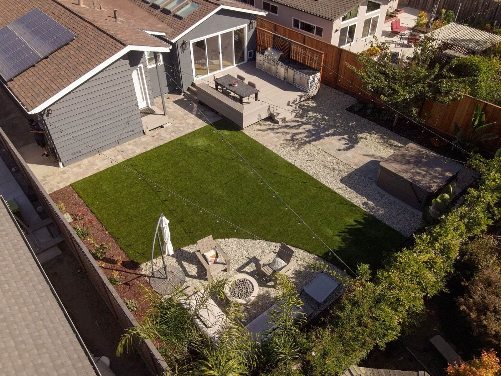 Residential backyard featuring outdoor kitchen, artificial turf lawn, fire pit seating area, and custom deck by K&D Landscaping