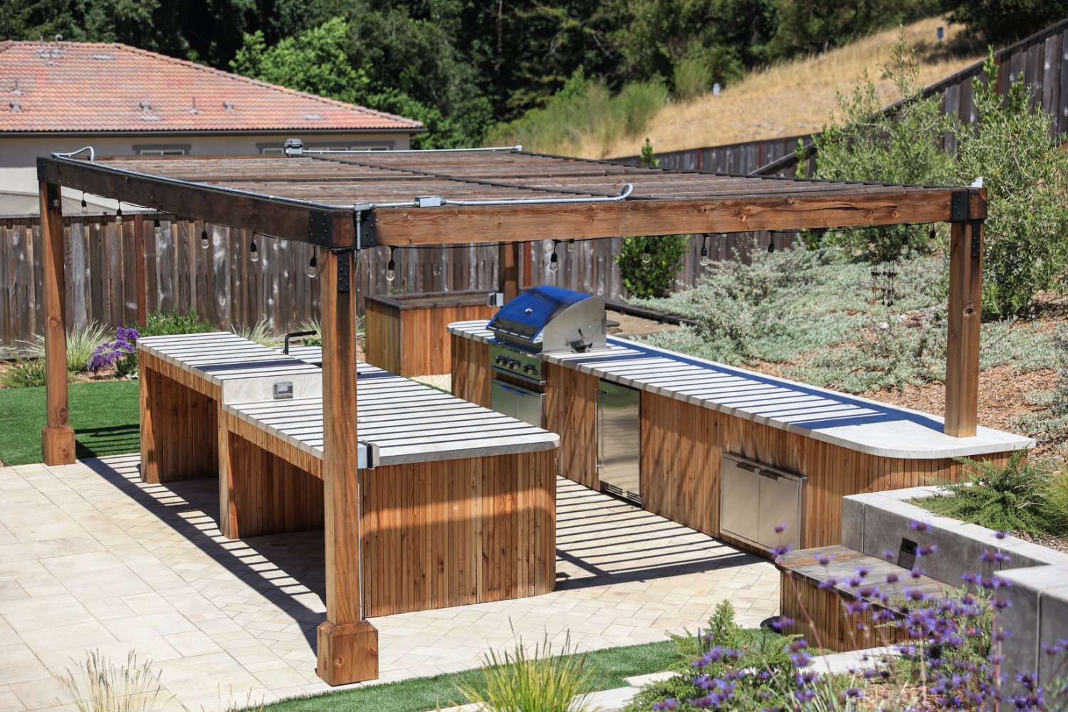 Residential backyard featuring pergola, lawn, and outdoor kitchen by K&D Landscaping