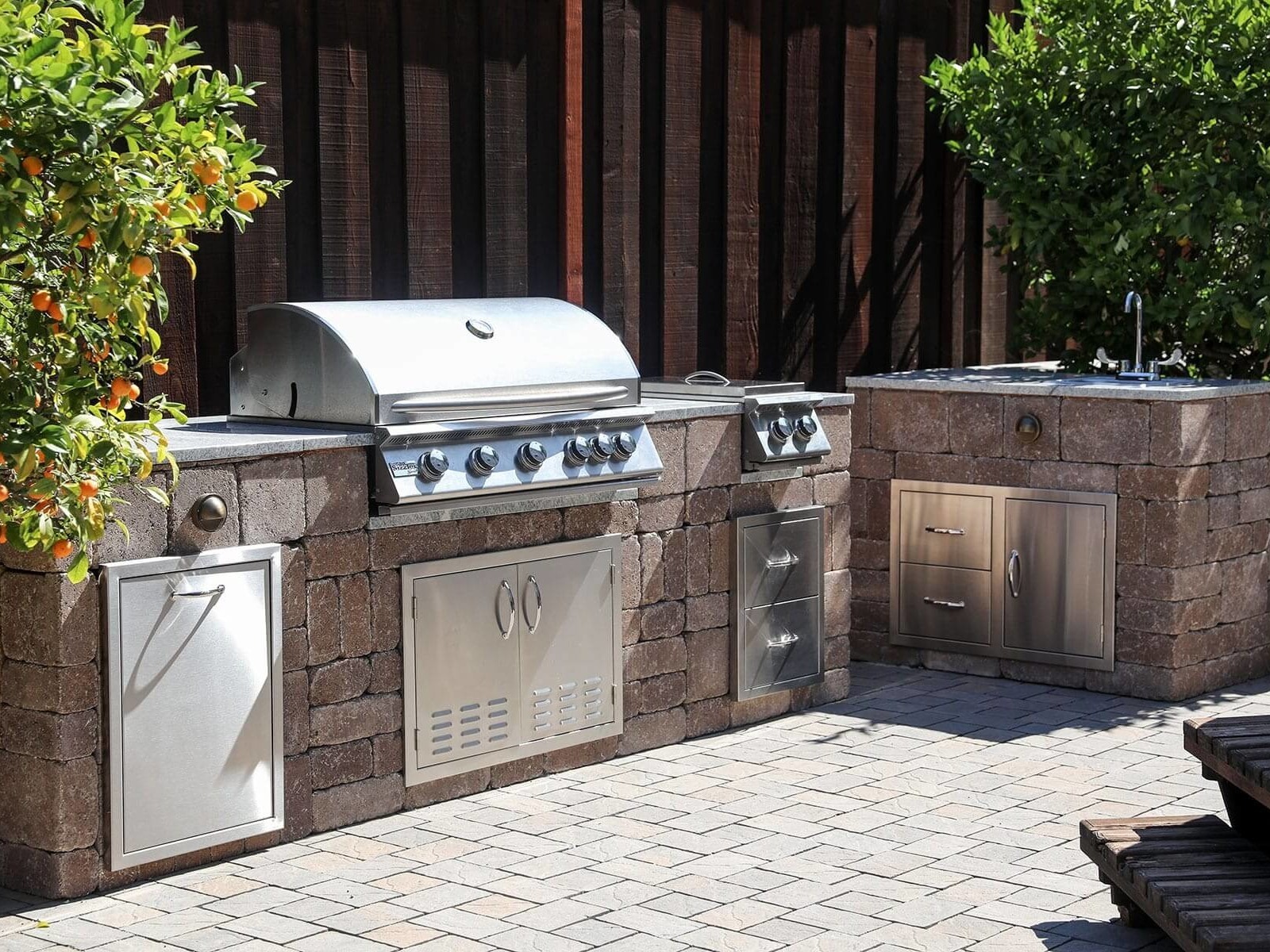 Backyard entertainment space with pavers and outdoor cooking area by K&D Landscaping