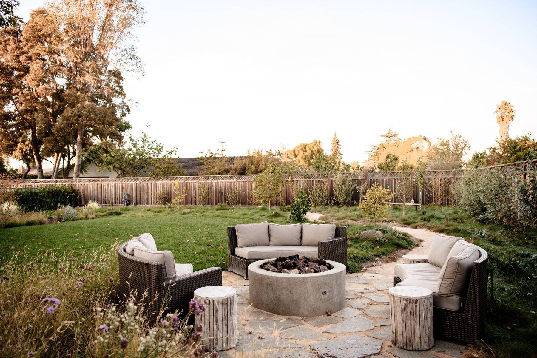 Backyard fire pit surrounded by ornamental grasses, landscape planting, and stone patio designed by K&D Landscaping