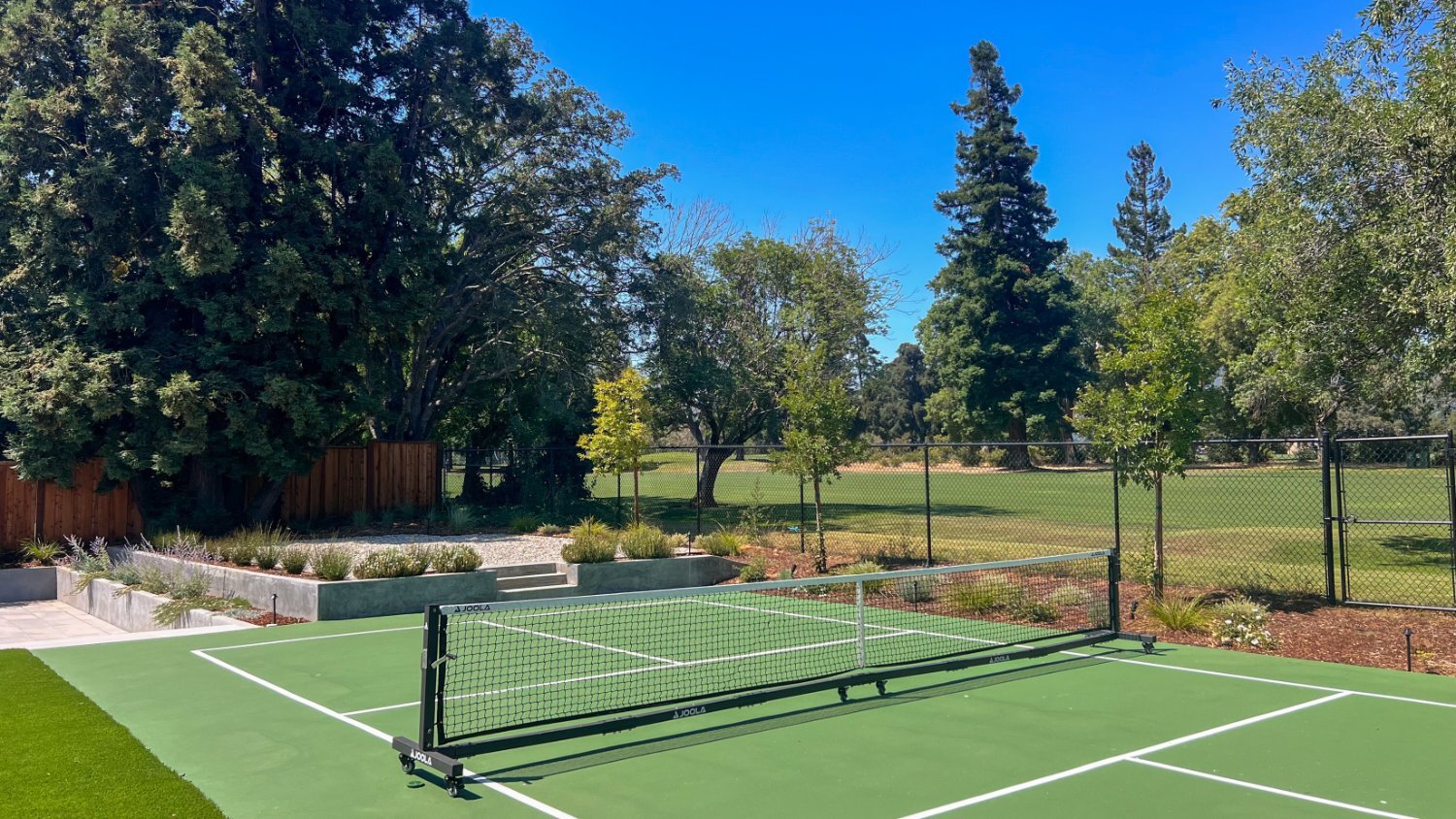 Backyard recreation area featuring pickleball court and outdoor gathering spaces by K&D Landscaping