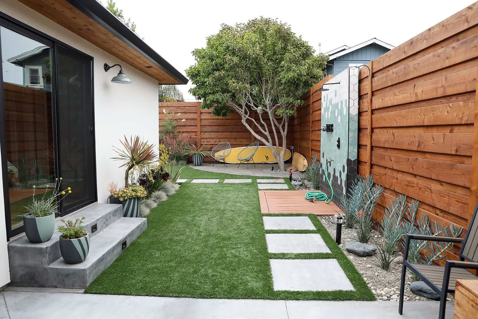 Backyard retreat with artificial turf, decking, and landscape lighting by K&D Landscaping