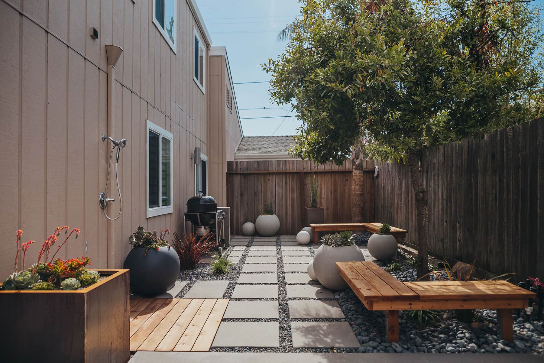 Complete backyard living space with modern structure, redwood fencing, concrete paver patio with gravel joints, white sphere planters, outdoor shower, and contemporary landscape installation by K&D Landscaping