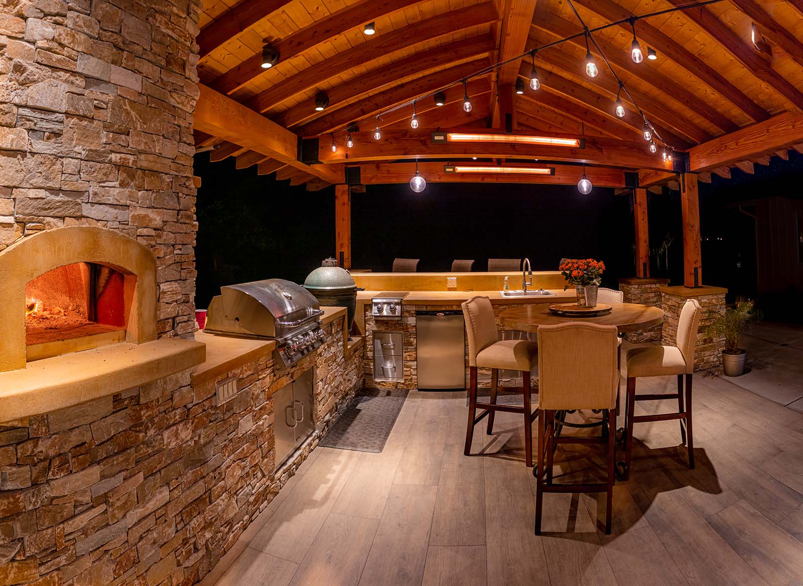 Custom outdoor kitchen with pizza oven, stone veneer finishes, and built-in cooking appliances by K&D Landscaping