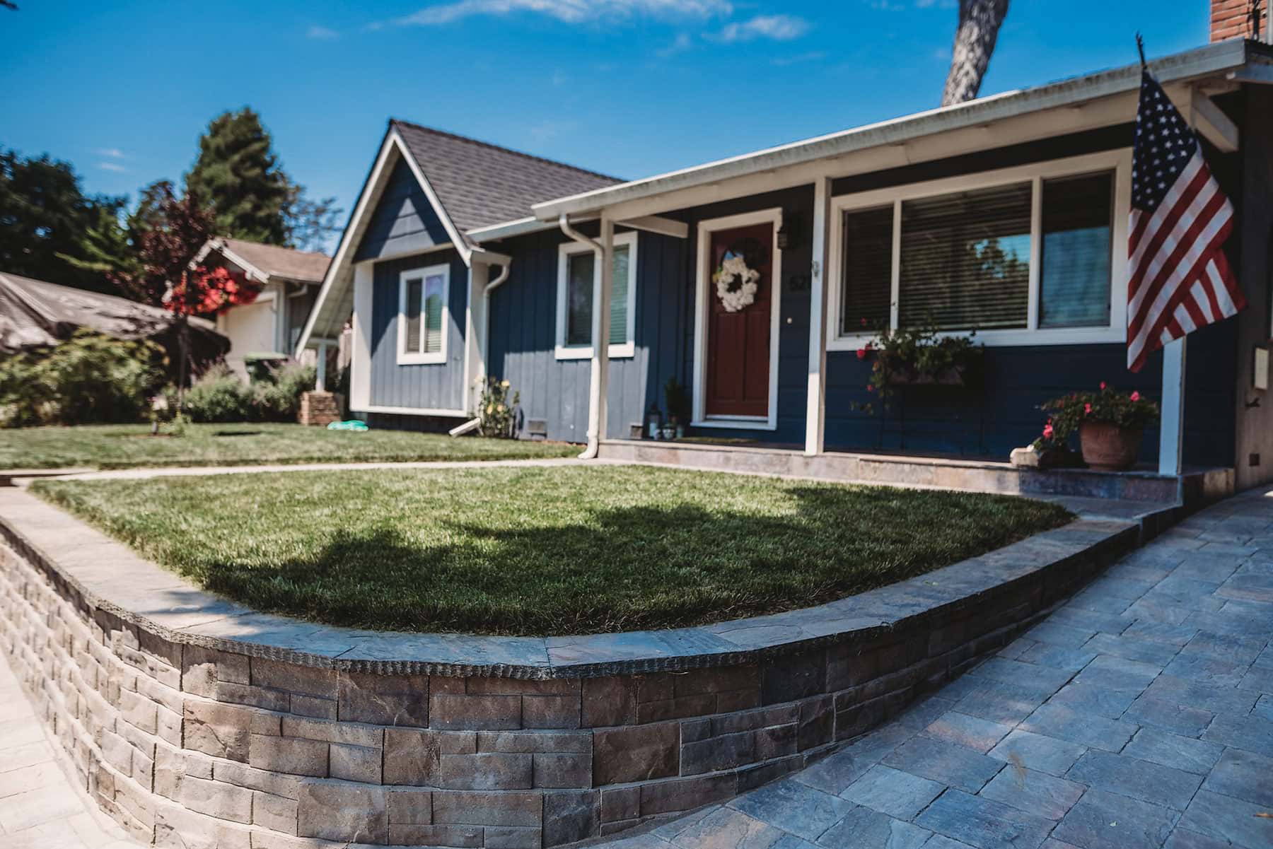 Front elevation of Aptos home with natural stone retaining wall, concrete steps, lawn, and landscaping by K&D Landscaping
