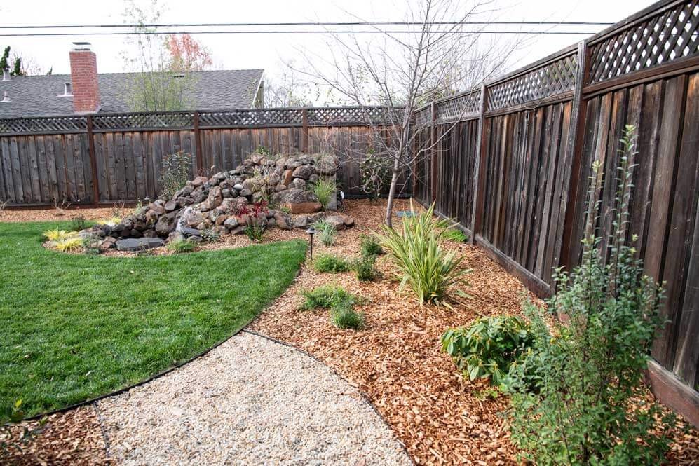 K&D Landscaping backyard corner with a boulder rockery, mulch beds and a decomposed-granite path