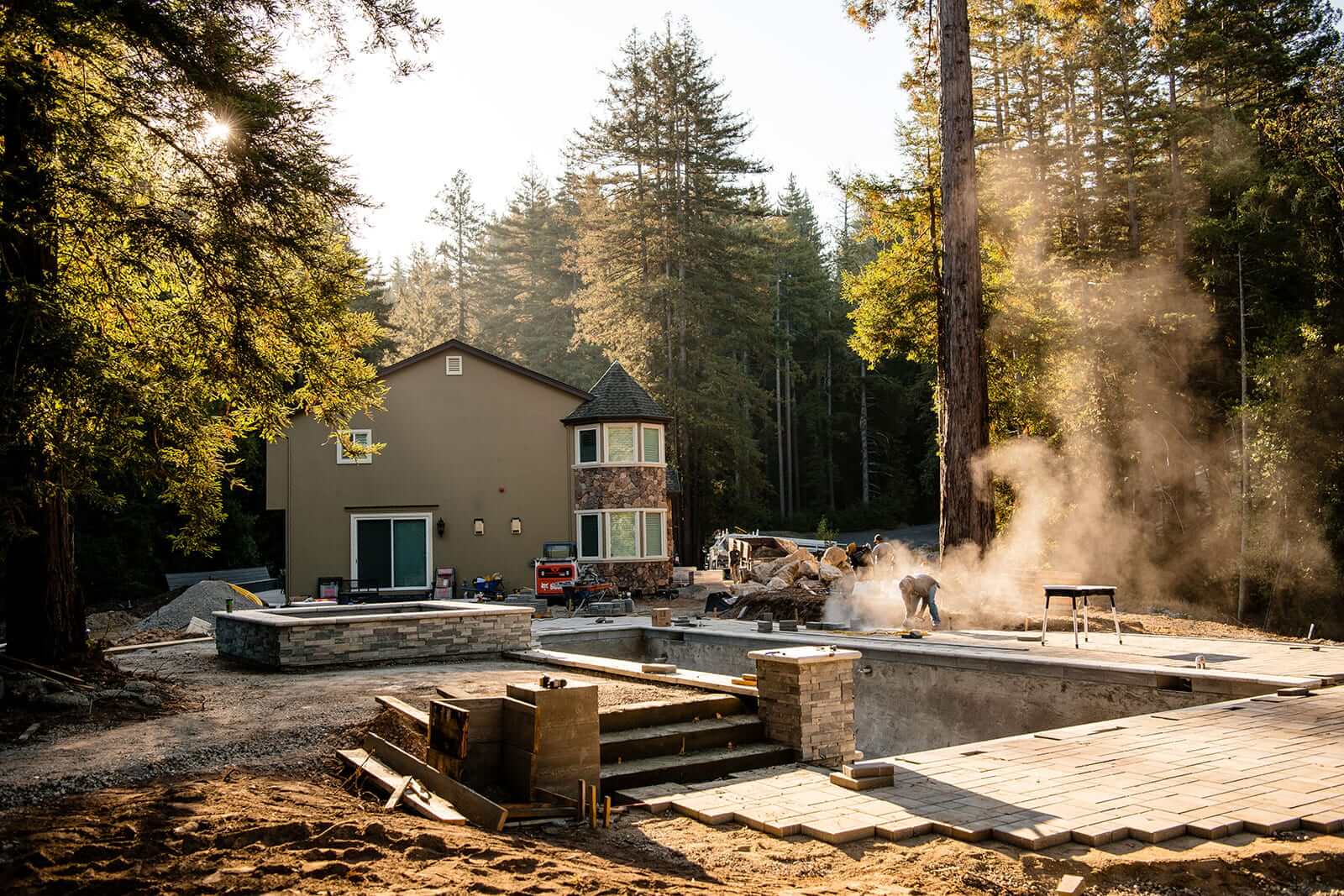 K&D Landscaping backyard mid-construction with an excavated pool and stacked-stone walls taking shape