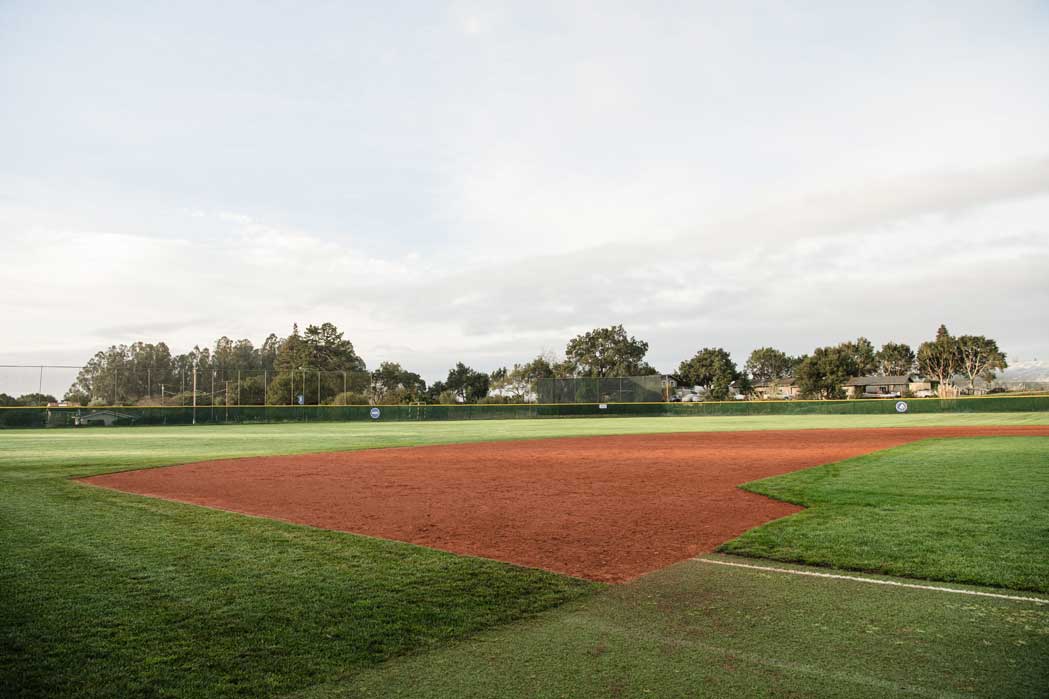 K&D Landscaping baseball diamond with a clay infield bordered by striped turf and an outfield fence