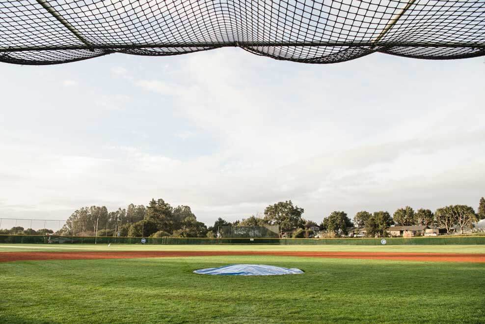 K&D Landscaping baseball field framed by the sagging backstop net with a tarp-covered mound