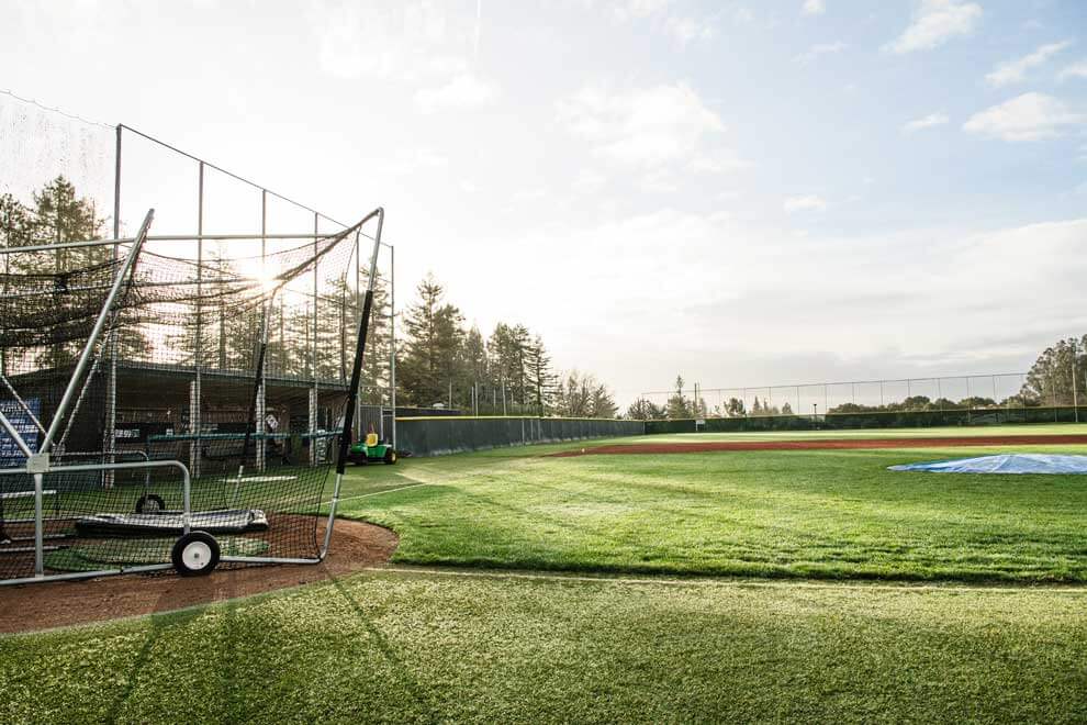 K&D Landscaping baseball field with a batting cage backstop and grounds equipment at sunrise