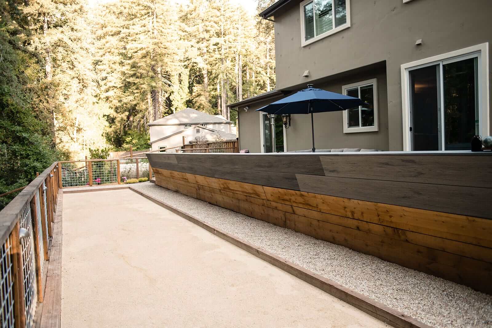 K&D Landscaping bocce court beside a stepped wood retaining wall and hog-wire railing below the house