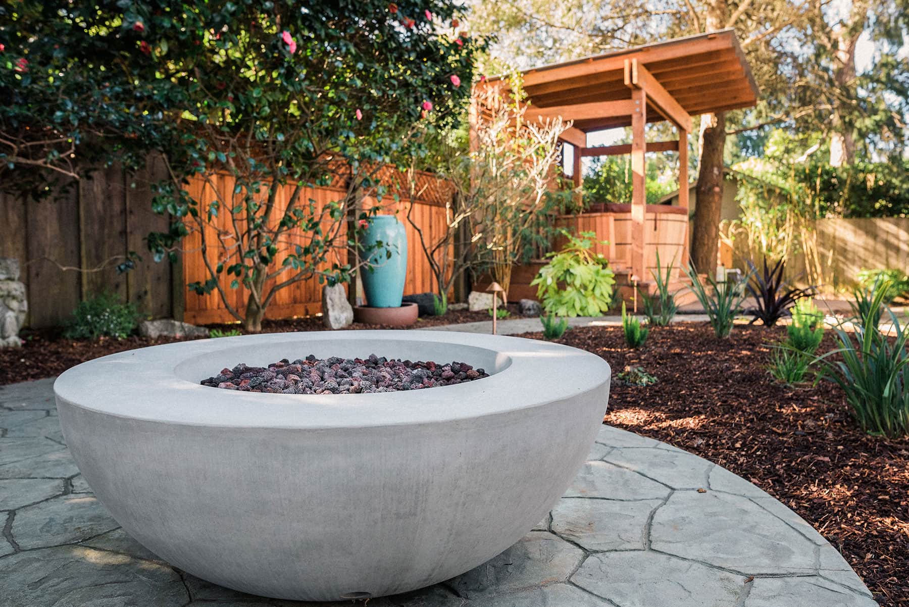 K&D Landscaping concrete fire pit bowl with gravel surround, native plantings, arbor, and outdoor living courtyard