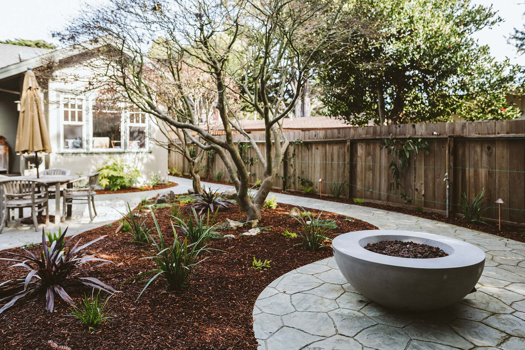 K&D Landscaping courtyard landscape with mature trees, fire pit, arbor, native plantings, and hardscape