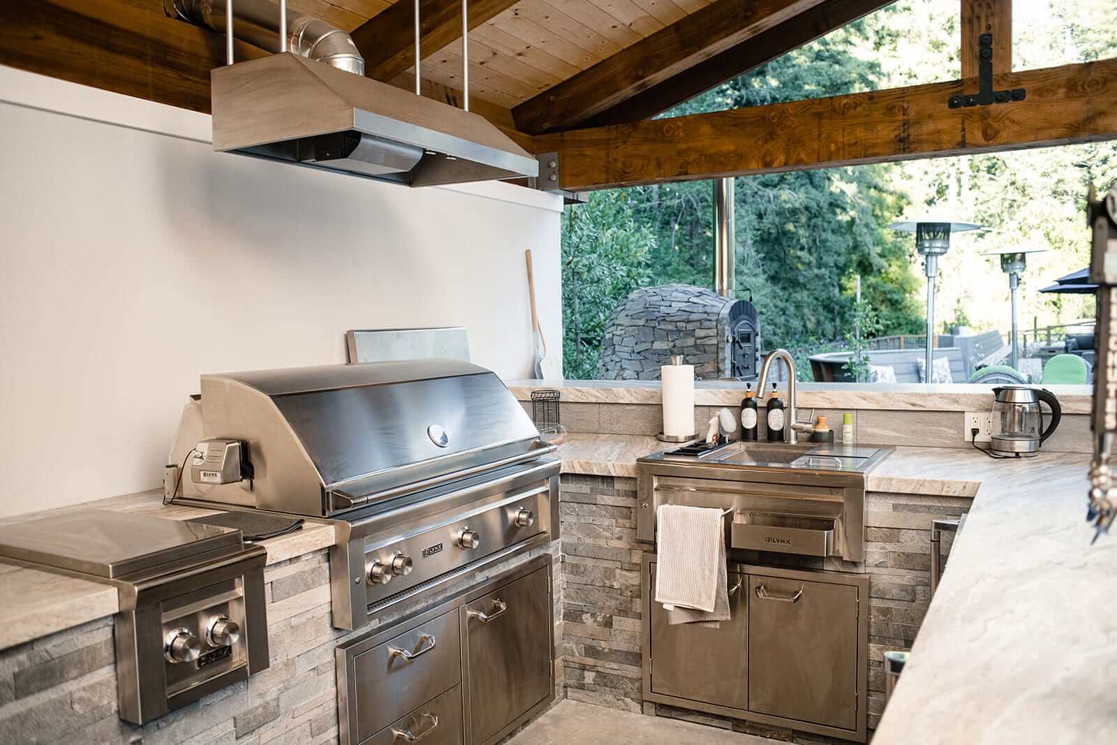 K&D Landscaping covered outdoor kitchen with a stainless grill, side burner, sink and stone counters