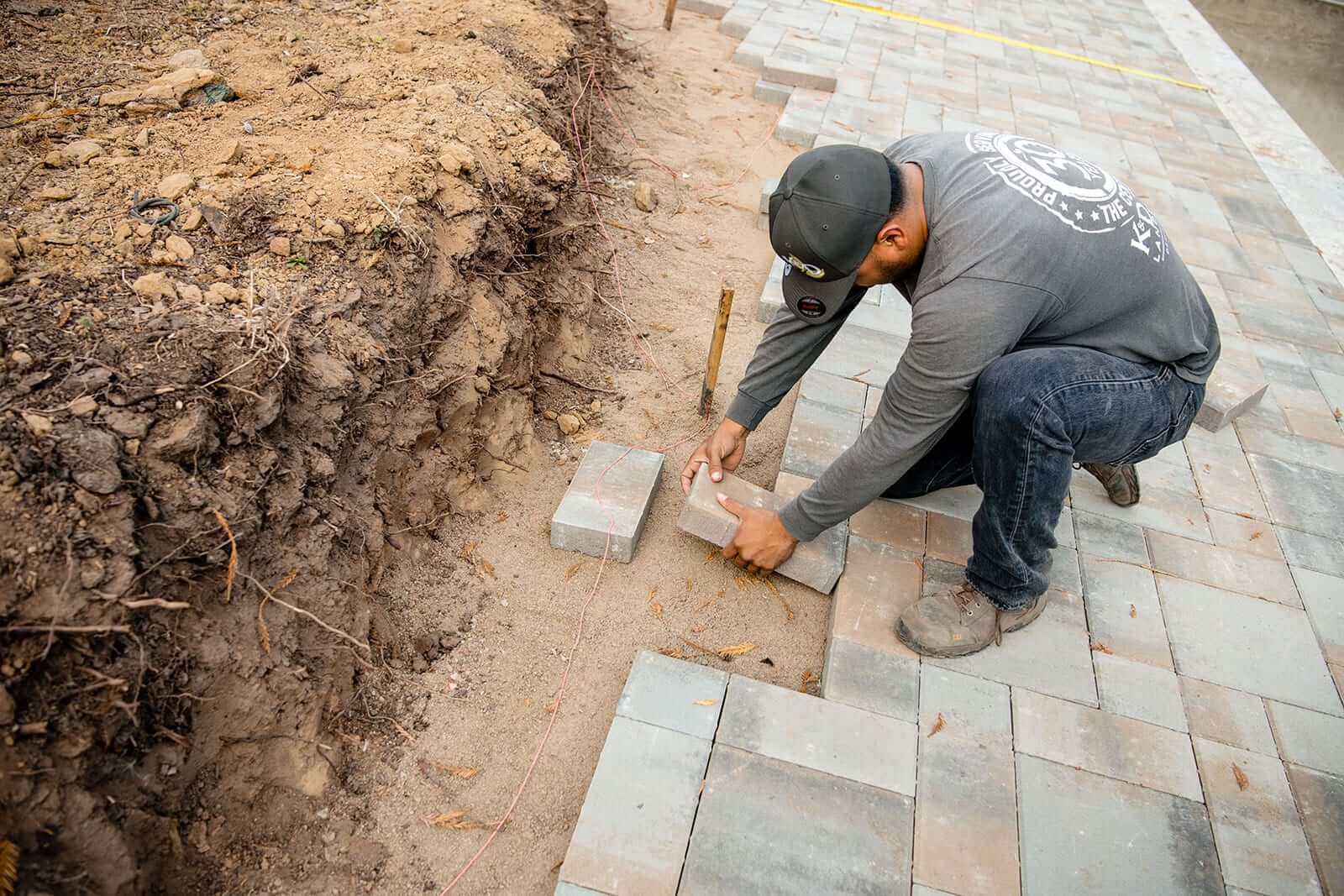 K&D Landscaping crew member setting pavers along a freshly excavated garden edge