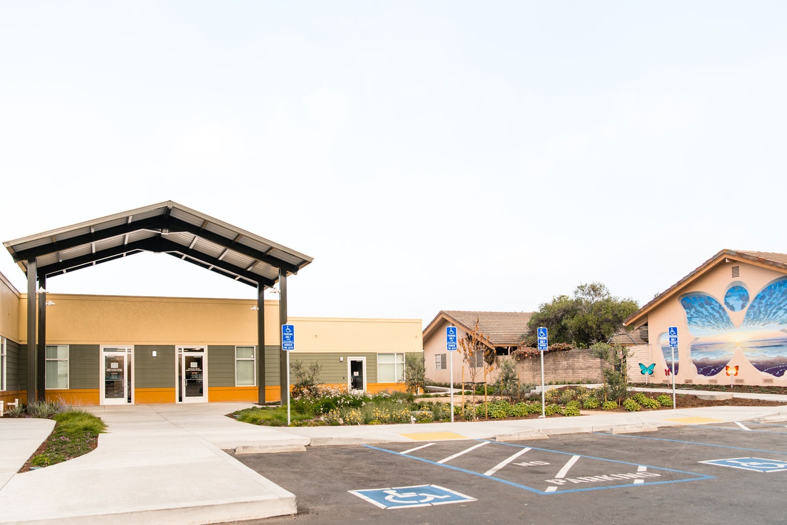 K&D Landscaping full site view featuring metal pergolas, butterfly art building mural, and comprehensive landscape installation