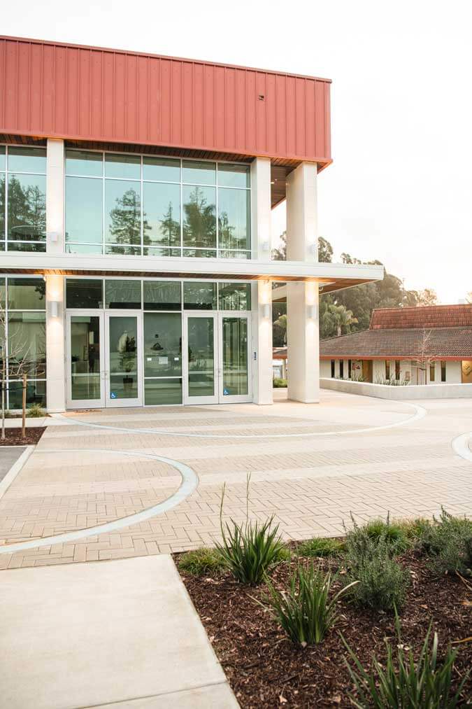 K&D Landscaping glass-walled building entrance with a herringbone paver plaza and drought-tolerant beds