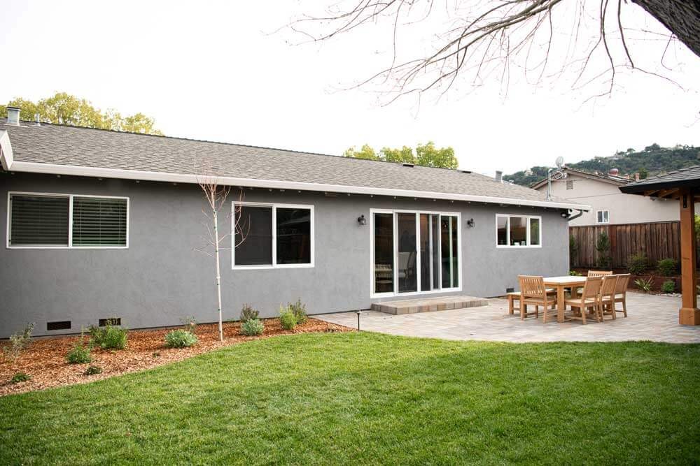 K&D Landscaping gray ranch home rear elevation with a paver patio dining area and fresh lawn