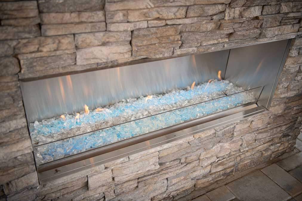 K&D Landscaping linear gas fire feature with blue fire glass set into a stacked-stone wall