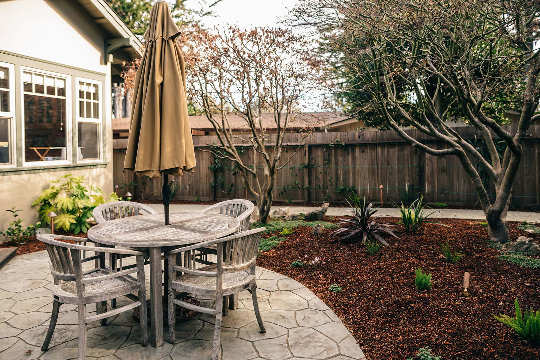 K&D Landscaping outdoor dining patio with round table, umbrellas, low voltage lighting, and native plantings