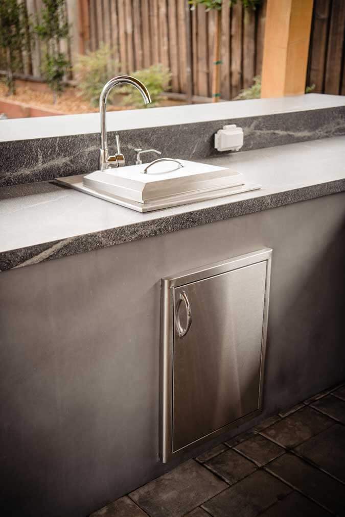 K&D Landscaping outdoor kitchen bar sink and stainless access door in a dark stone counter