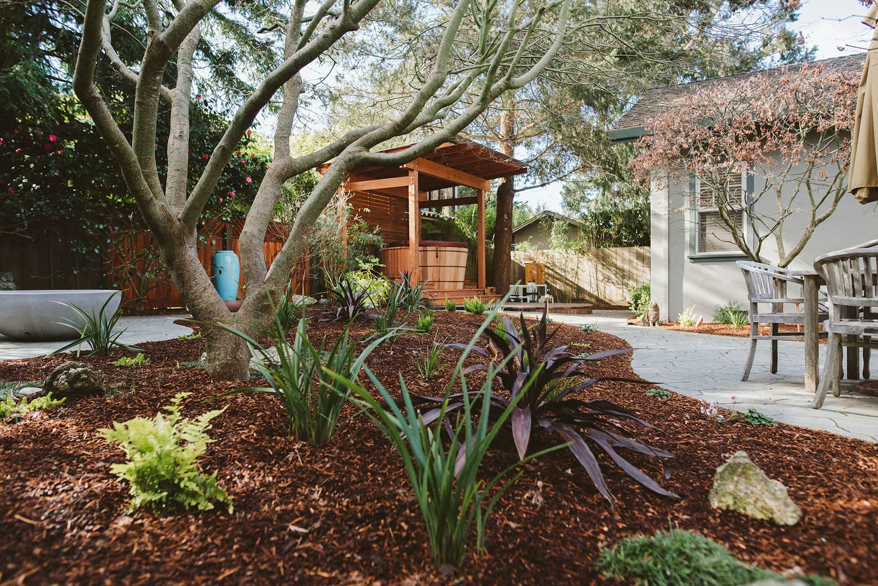 K&D Landscaping outdoor living space with hot tub deck, arbor, fire pit, mulch beds, and tree canopy