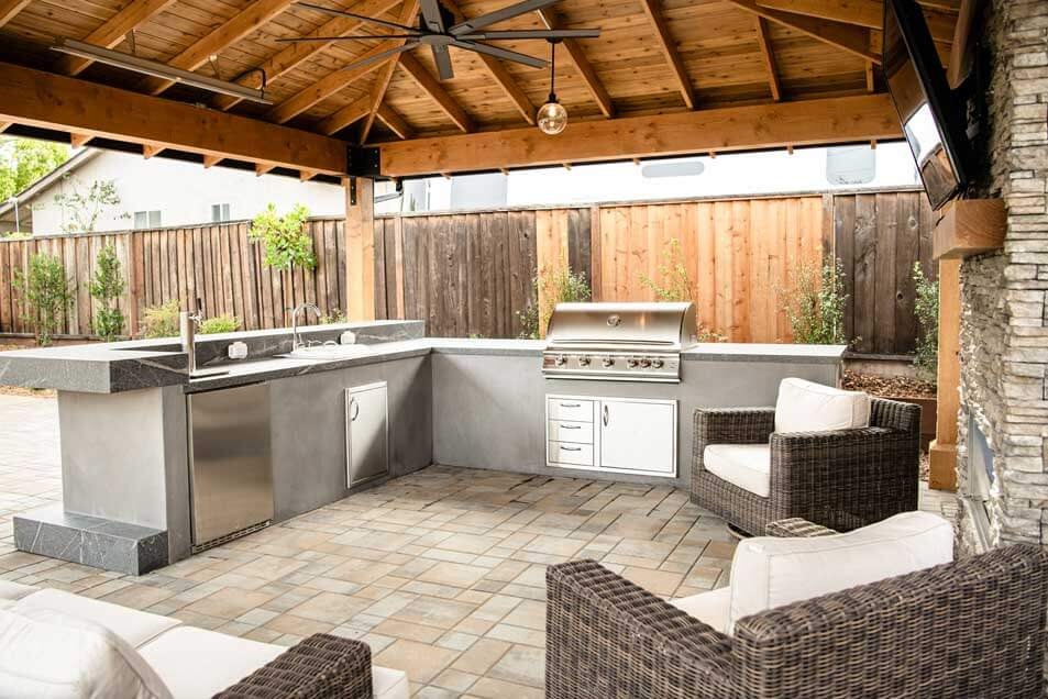 K&D Landscaping paver patio with a cedar pavilion, teak dining set and an outdoor kitchen and fireplace