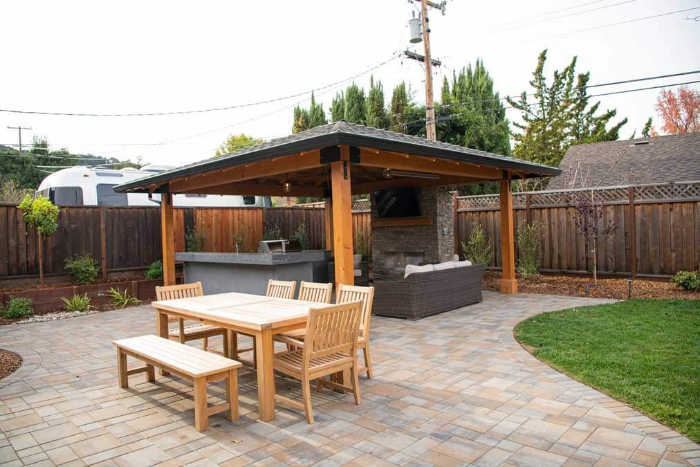 K&D Landscaping paver patio with a cedar pavilion, teak dining set and an outdoor kitchen and fireplace