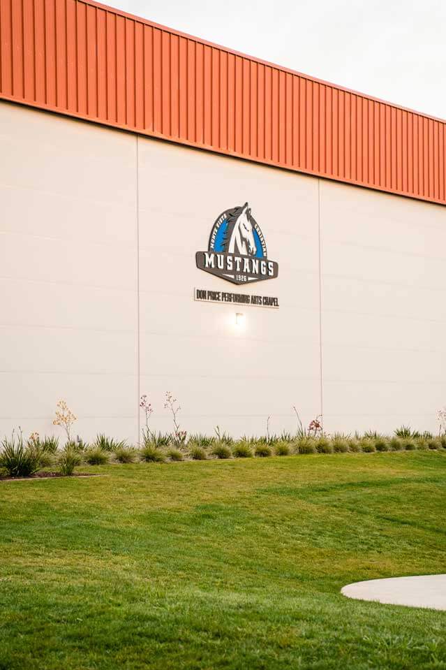 K&D Landscaping performing arts chapel wall with the Mustangs logo above an ornamental grass border