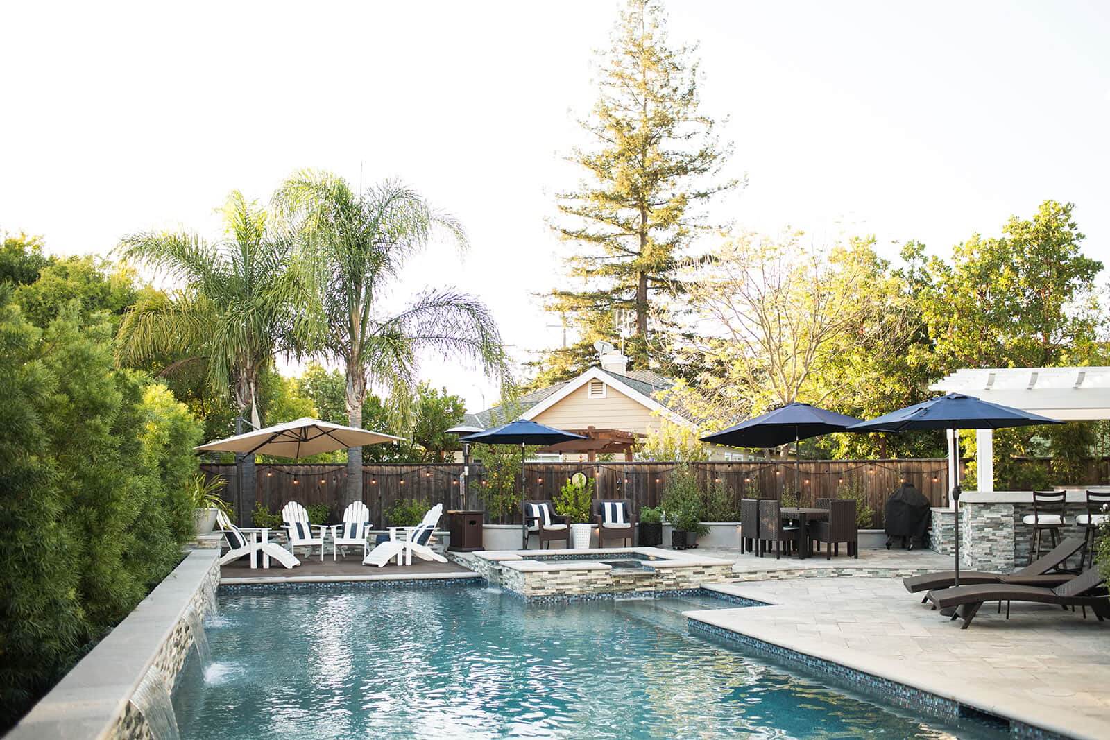 K&D Landscaping pool and spa surrounded by paver patio, pergolas, and outdoor living spaces