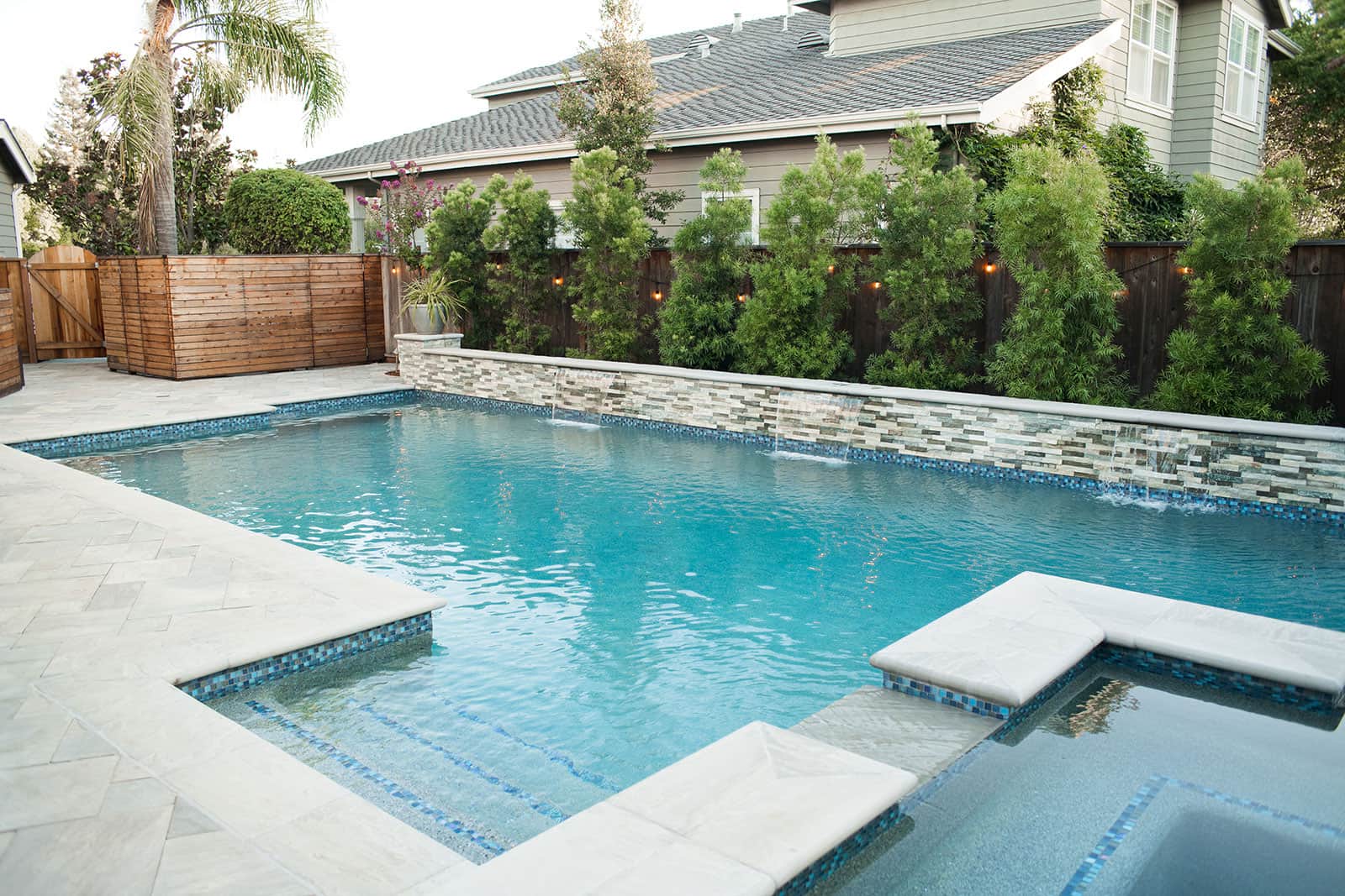 K&D Landscaping raised planter wall with stone veneer, decorative planters, and pool feature