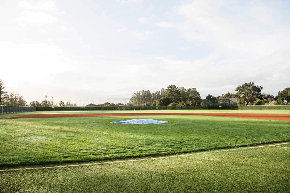 K&D Landscaping sunlit baseball field with a covered pitching mound and chalked foul line