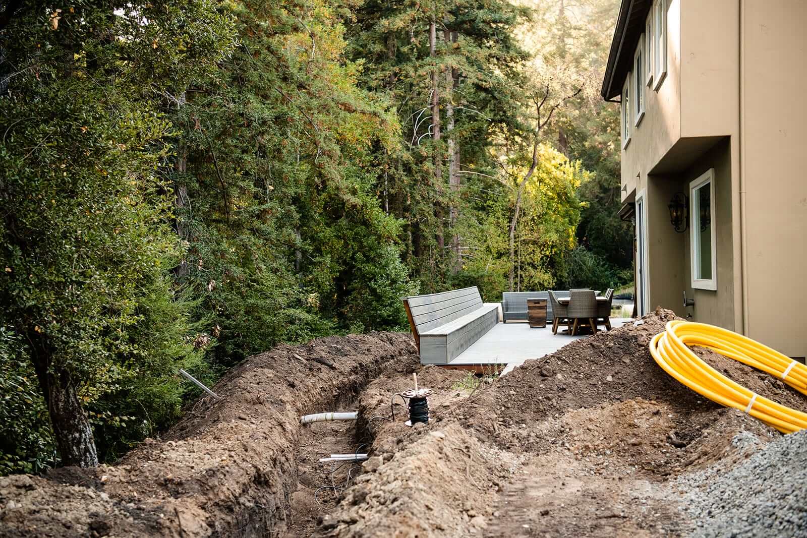 K&D Landscaping utility trench with conduit and a coiled gas line during installation beside a finished bench