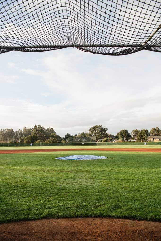 K&D Landscaping view through the backstop net to a grass infield and covered pitching mound