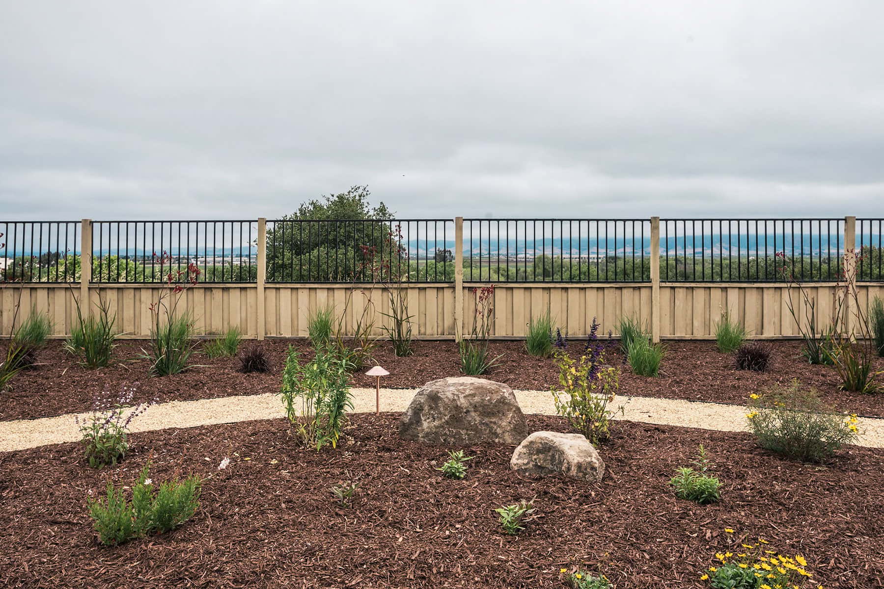 Landscape planting bed with curving gravel walkway, low-water perennials, decorative boulders, and native plantings installed by K&D Landscaping