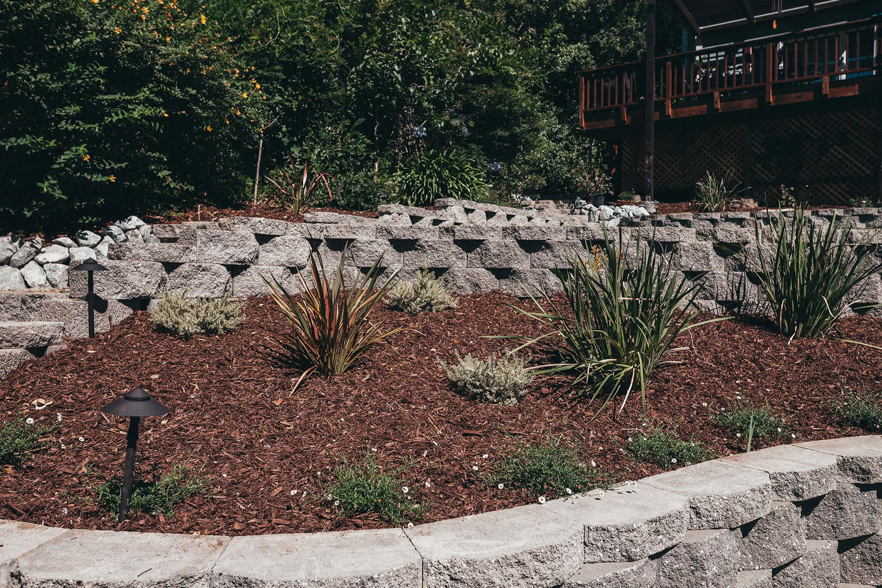 Landscape planting beds with natural stone walls, ornamental grasses, mulch, and low voltage lighting by K&D Landscaping