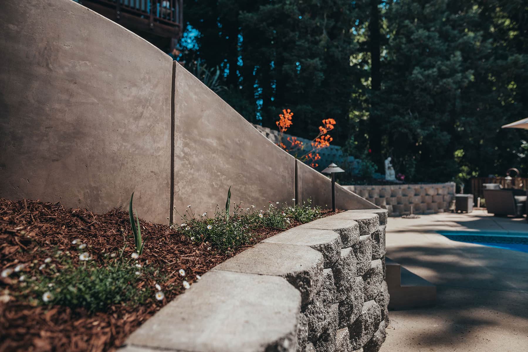 Modern concrete retaining wall with mulch landscape bed, decorative plantings, and drainage solutions by K&D Landscaping