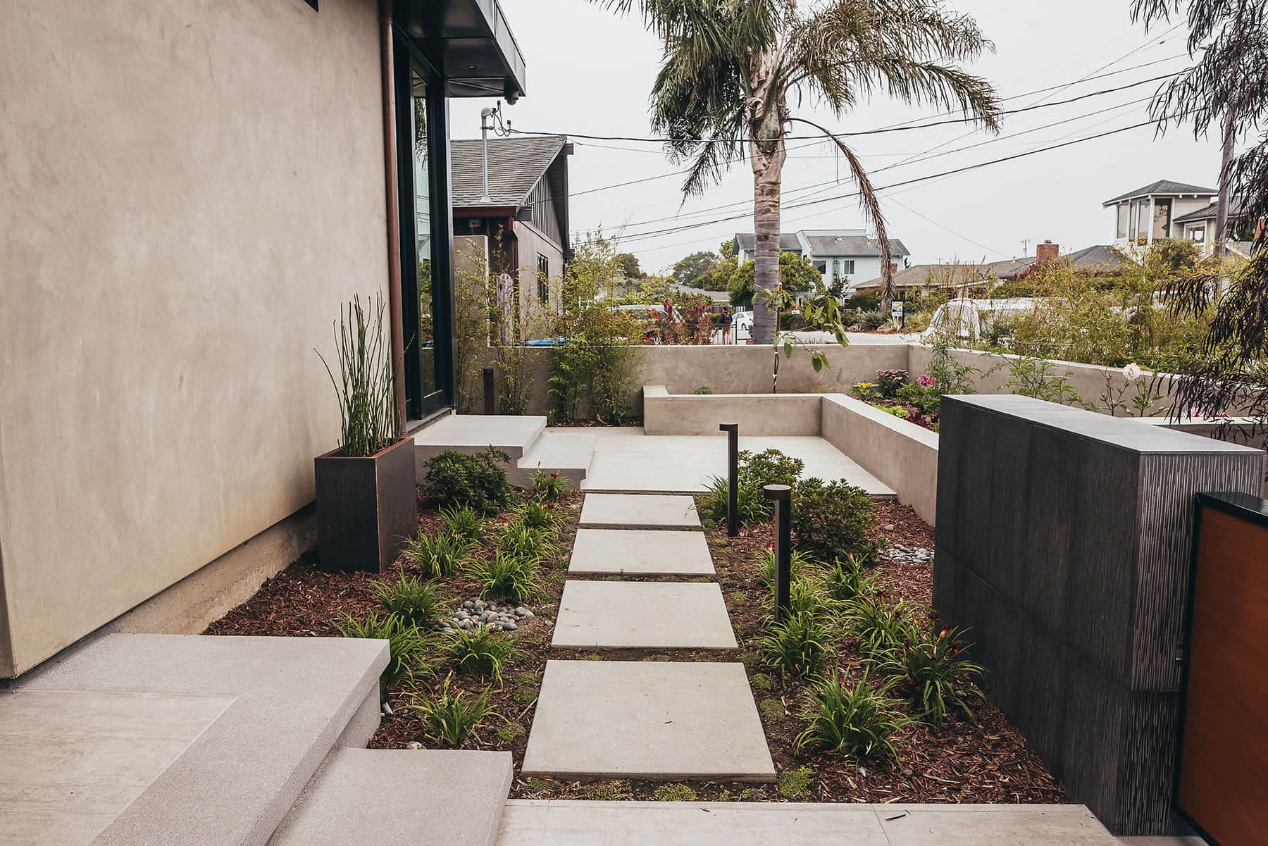 Modern concrete stepping stone pathway with raised planting beds, flowering plants, and mulch landscape design by K&D Landscaping