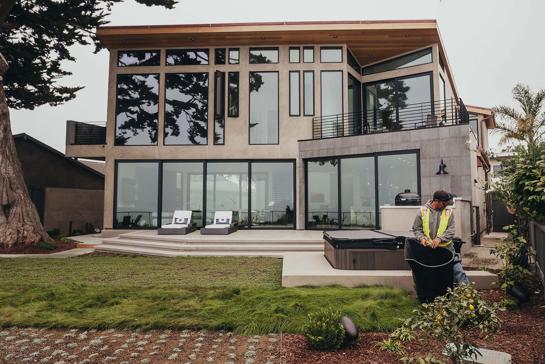 Modern oceanview landscape with concrete patio, manicured lawn, natural stone walls, and contemporary architecture by K&D Landscaping