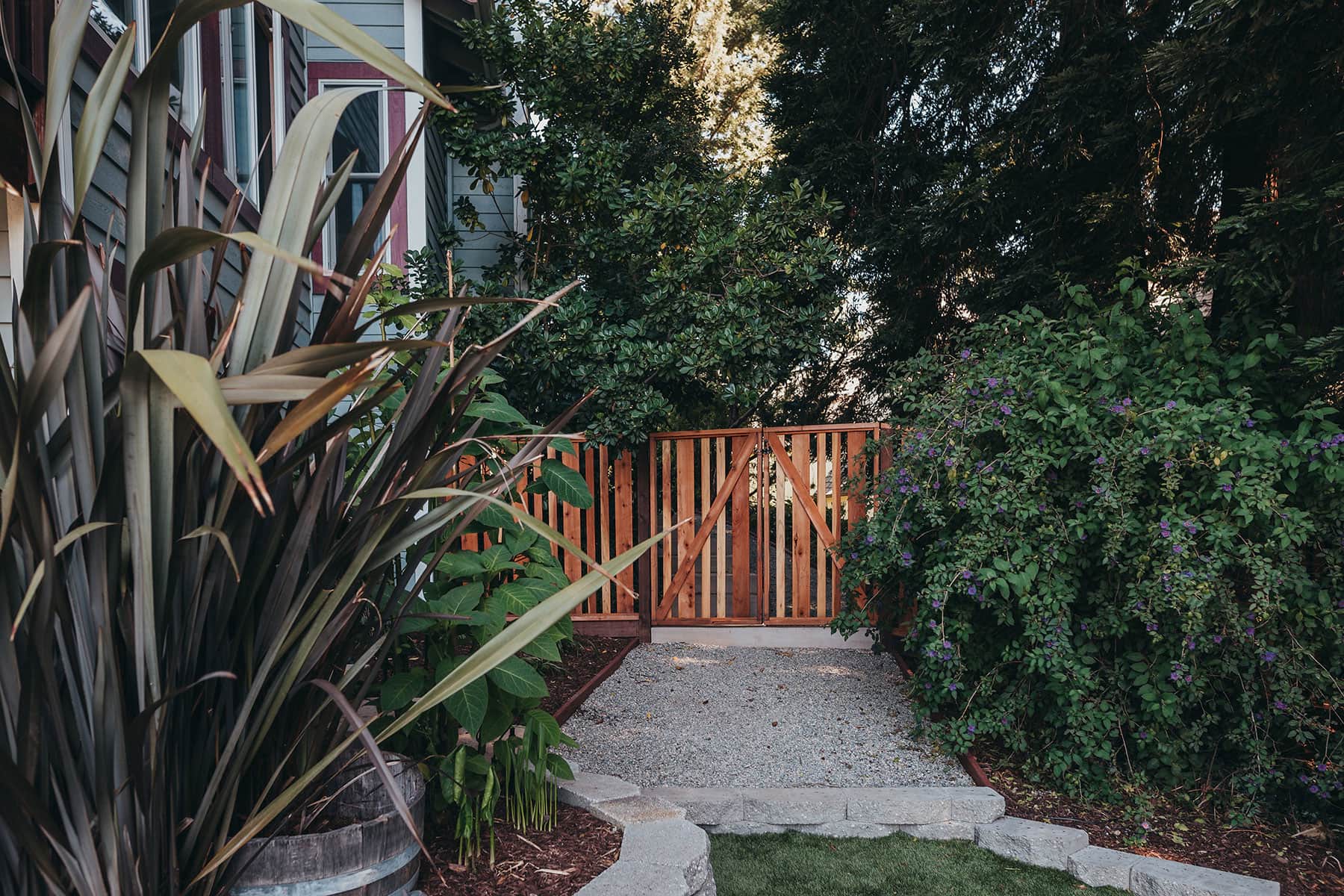 Ornamental grass planting with redwood gate entrance, mulch groundcover, and gravel pathway installed by K&D Landscaping