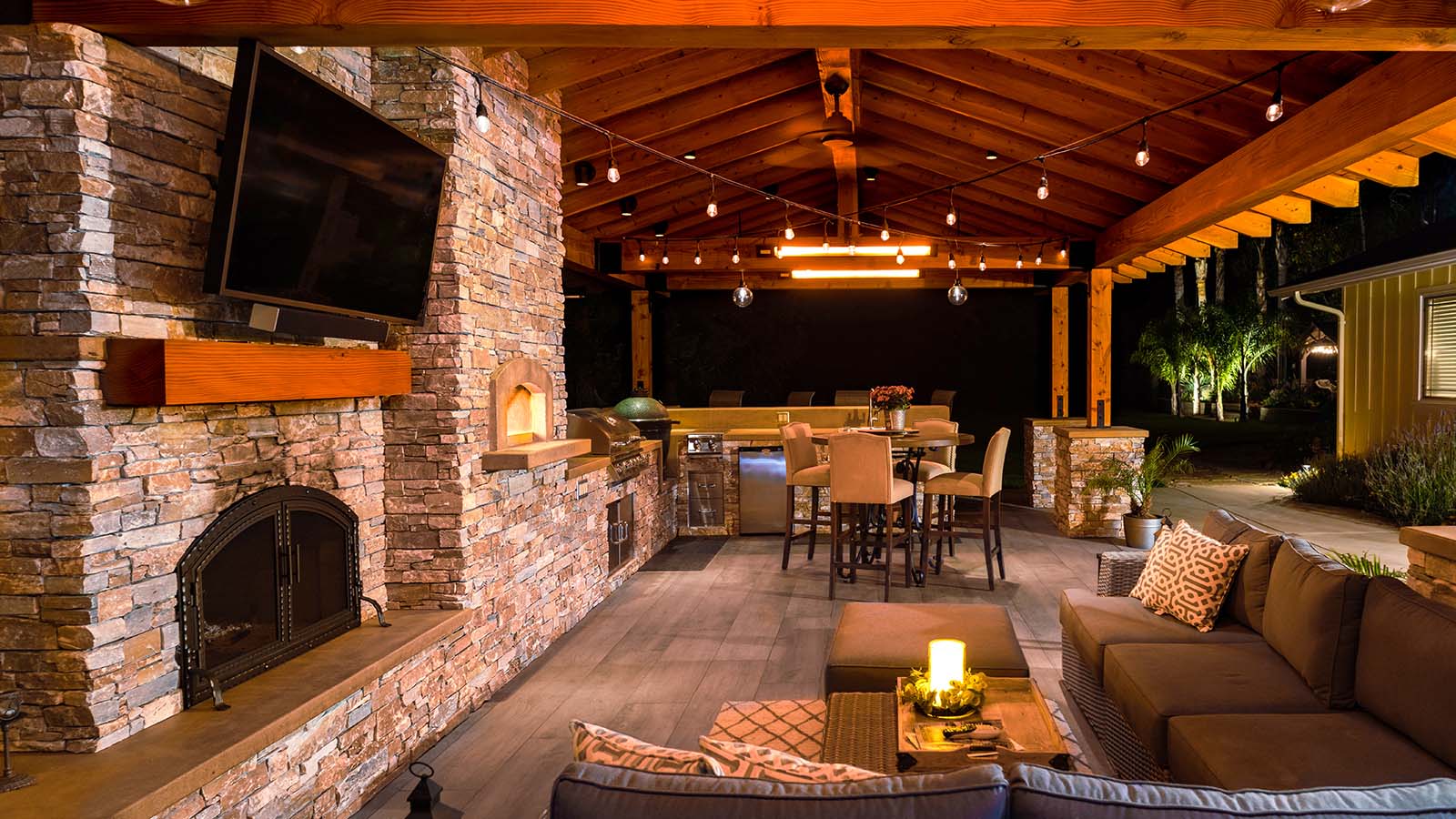 Outdoor entertaining space with fireplace, lounge seating, and custom stone kitchen by K&D Landscaping