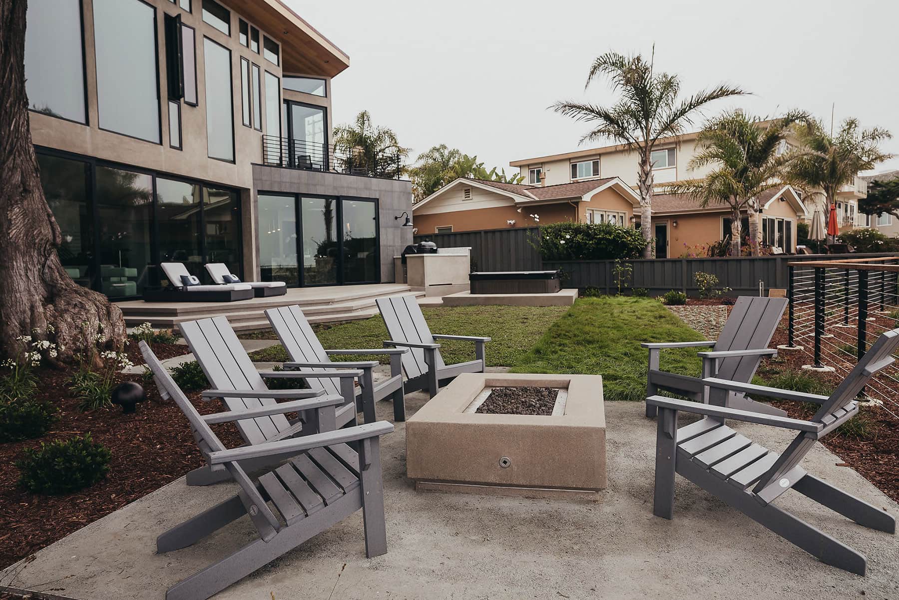 Outdoor living area featuring fire feature, seat walls, Adirondack furniture, and modern landscape planting installed by K&D Landscaping