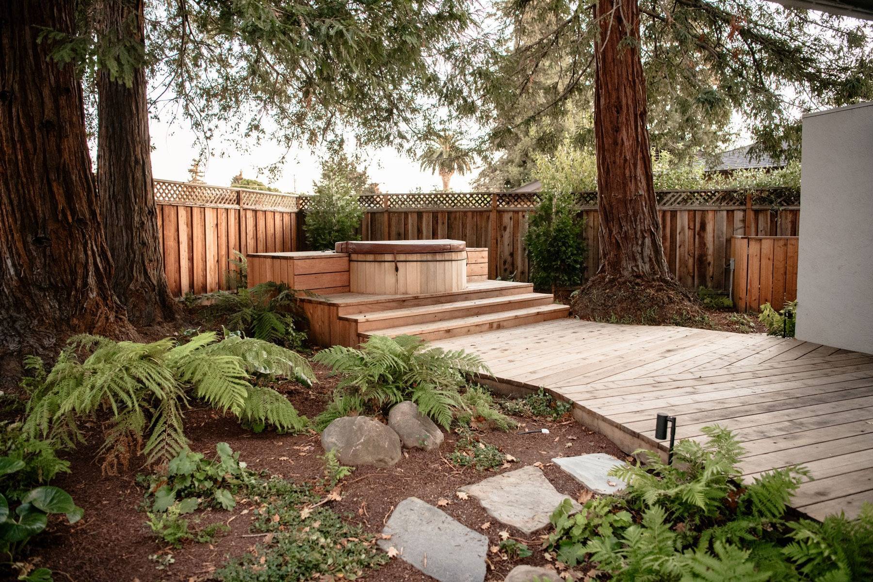 Pergola-covered outdoor kitchen and dining space with grill station, bar seating, and landscape design by K&D Landscaping