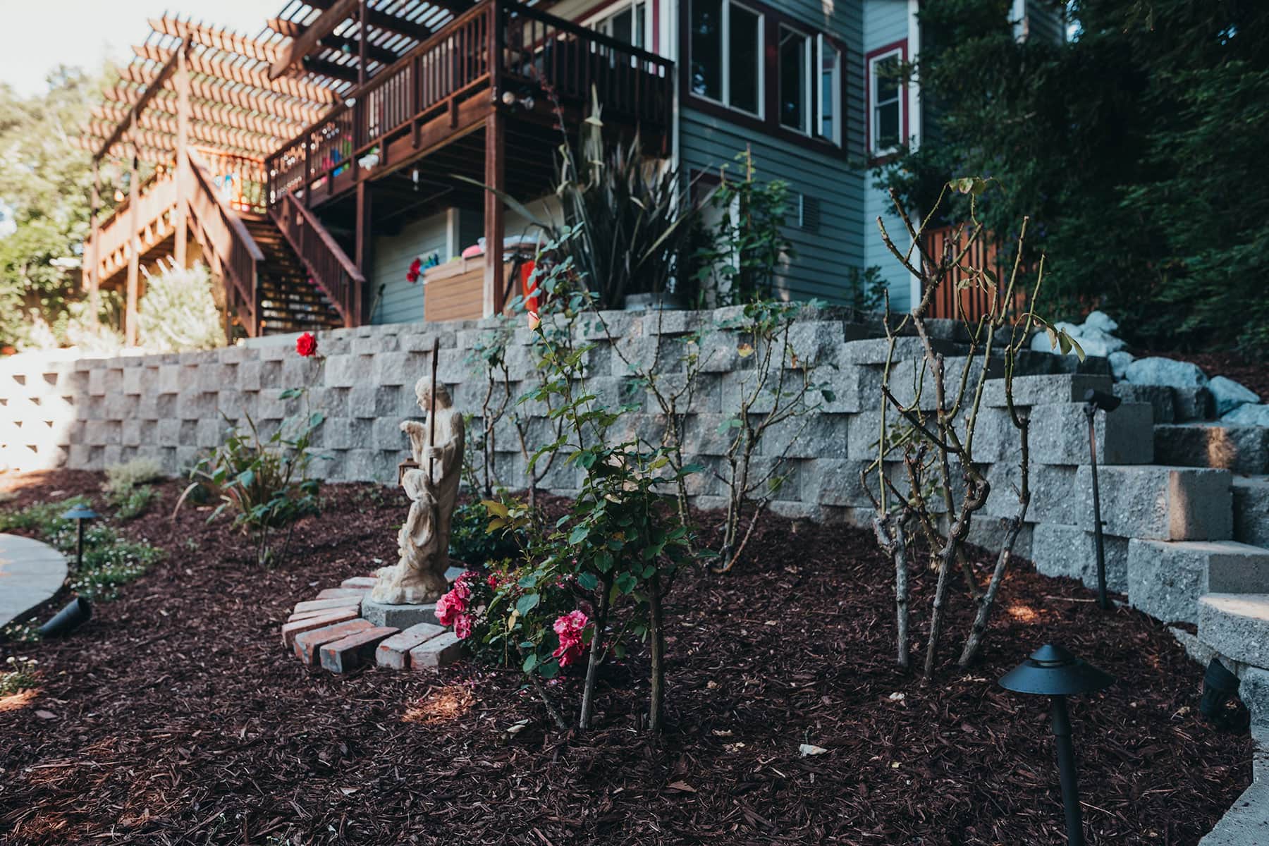 Planter boxes with blooming flowers, mulch landscape bed, natural stone wall, and redwood structure by K&D Landscaping