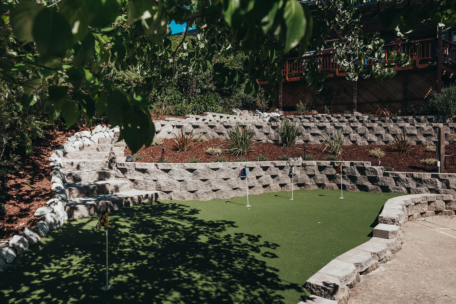 Putting green with ledge stone retaining walls, flowering shrubs, mulch groundcover, and shade created by K&D Landscaping