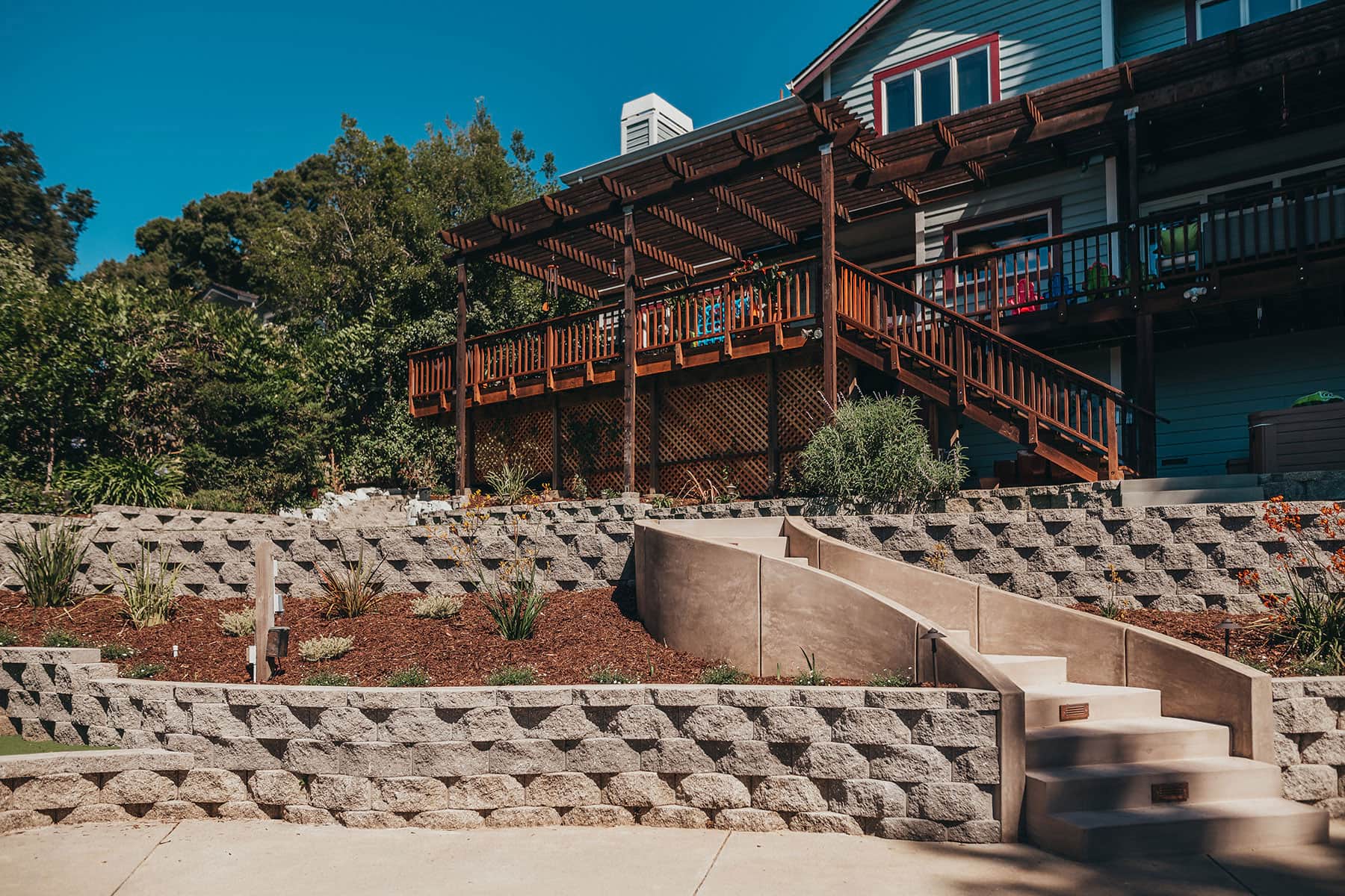 Redwood pergola structure overlooking backyard staycation with natural stone retaining walls and native planting by K&D Landscaping